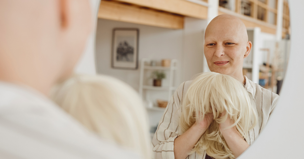 Bald woman holding a blonde wig in front of a mirror