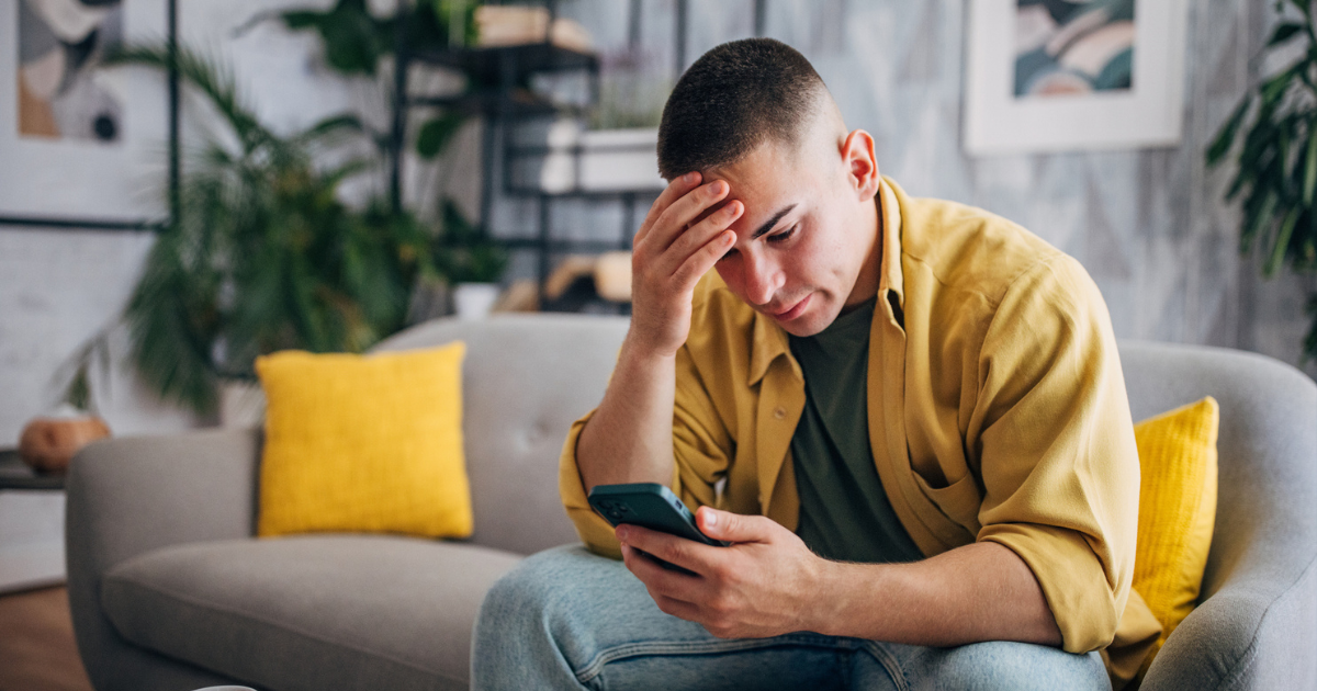 An individual is looking worried while browsing his smartphone , seated with a coffee cup on the table in a peaceful home setting