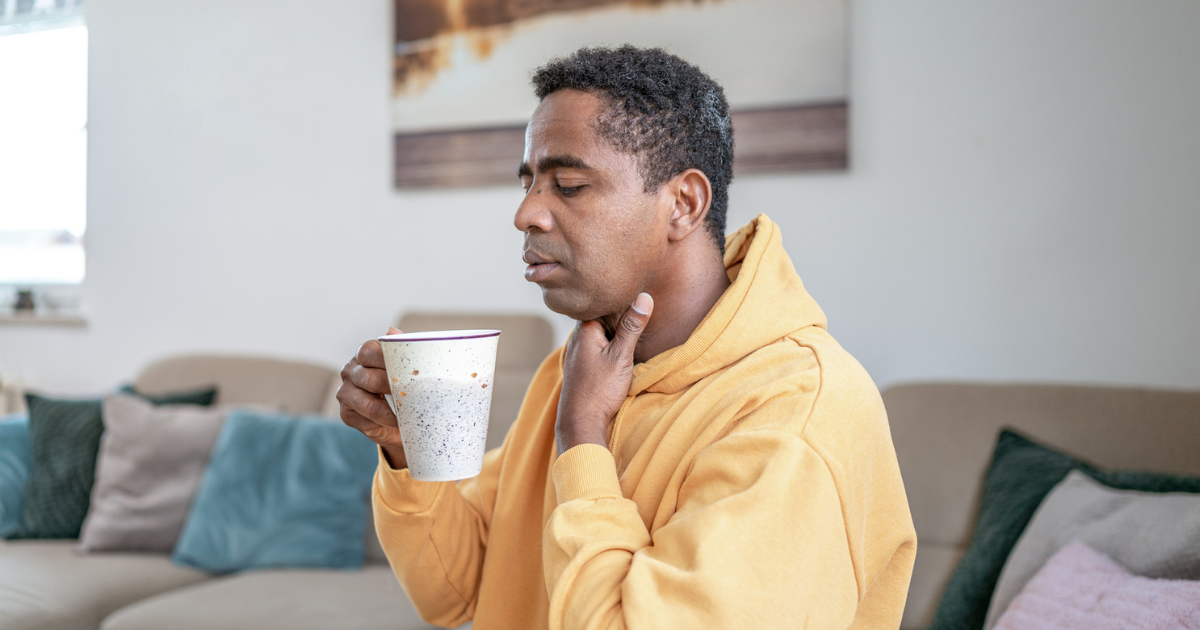 Man holding a cup of tea and touching his sore throat