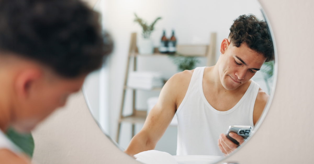 Young man in mirror holding smartphone.