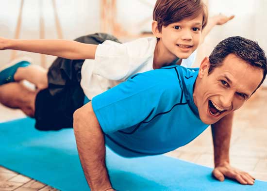 A man doing push ups while his son lays on the man's back pretending to be an airplane.