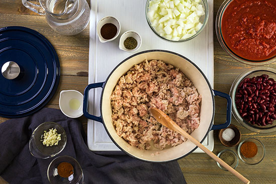 A blue pot filled with ground turkey, with small bowls of other ingredients surrounding it.