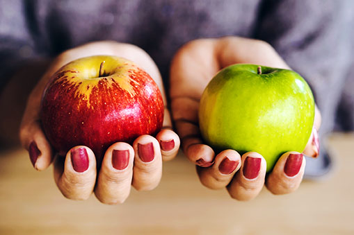 Close-up of two hands, with red painted nails, holding two apples.