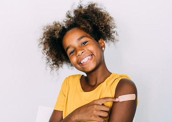 A little girl pointing to a band aid on her arm. 