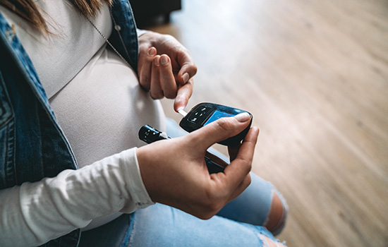 A pregnant woman measuring her blood sugar levels with glucose monitor.