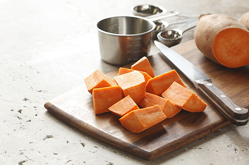 Chopped sweet potatoes and a butcher knife on a cutting board. 