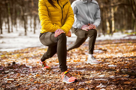 Women wearing running gear stretching in a wooded area. 