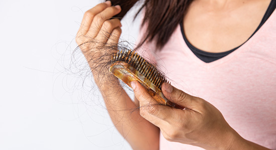 A woman looking at a hair brush full of hair. 