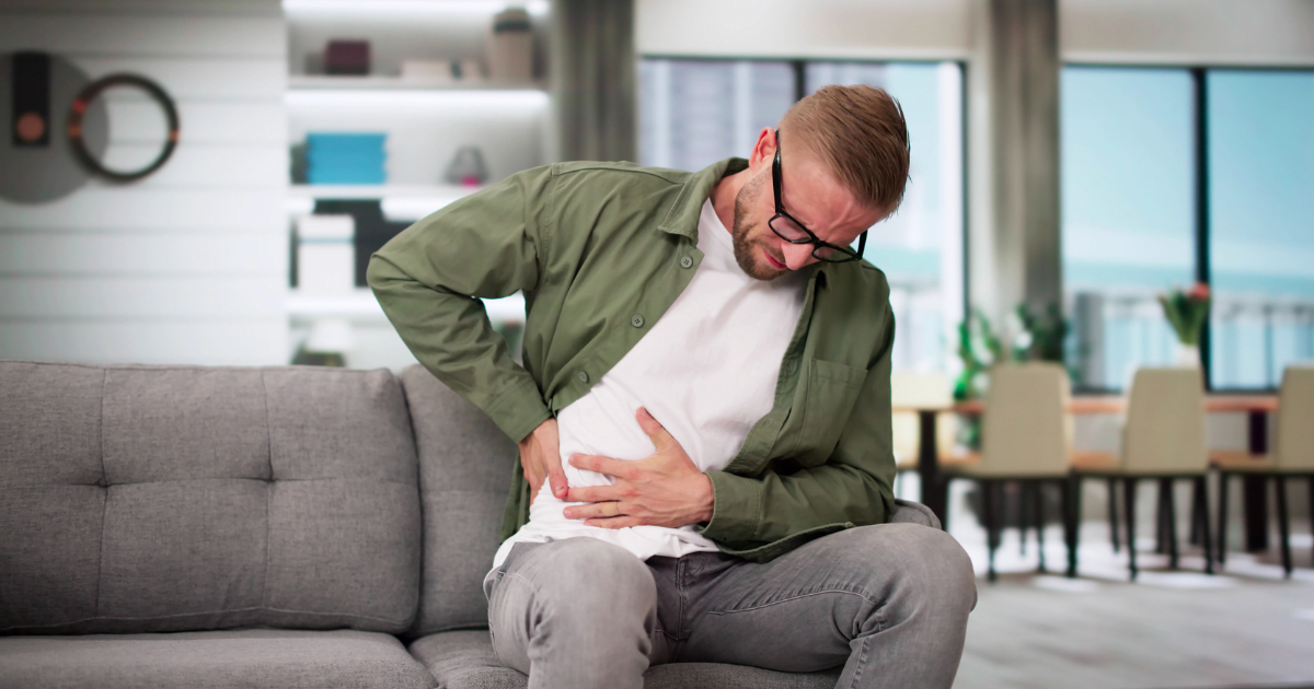 Man sitting on couch, holding abdomen in pain