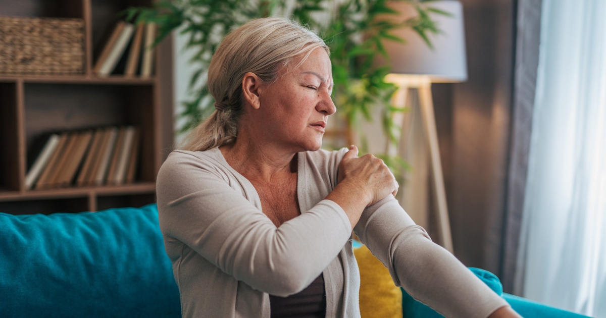 Woman sitting on couch holding arm in pain