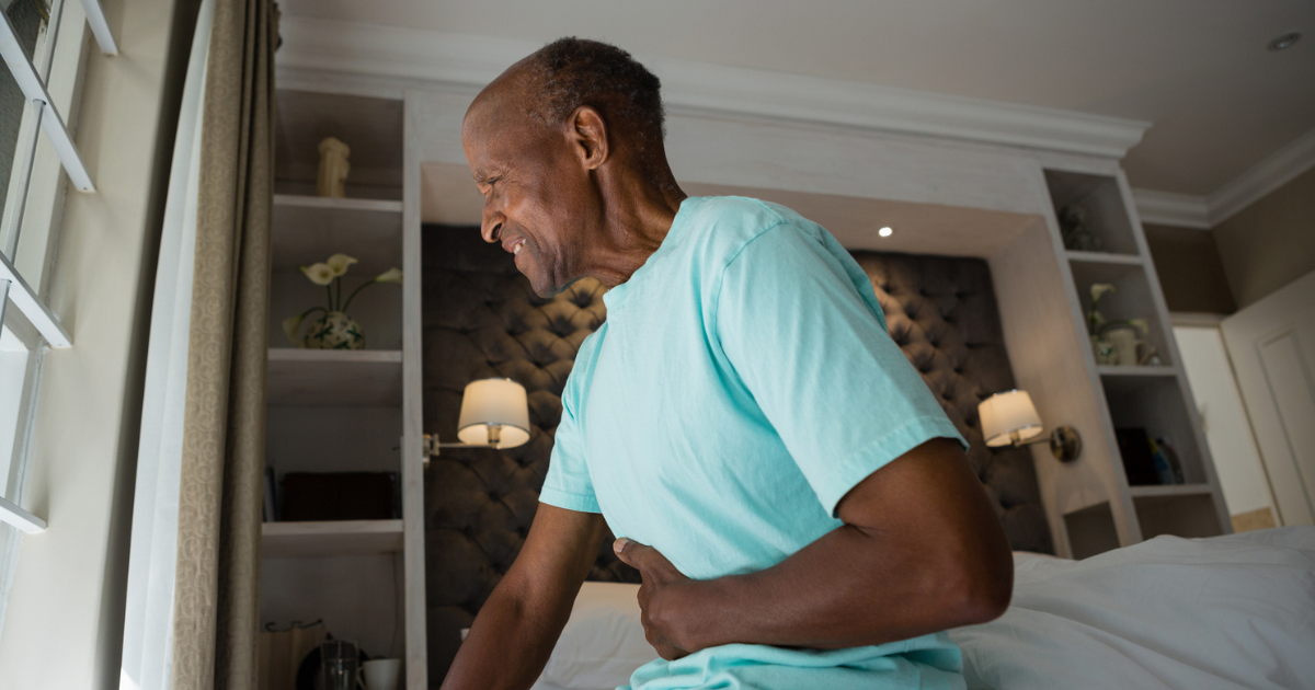 Older man sitting on his bed holding his stomach