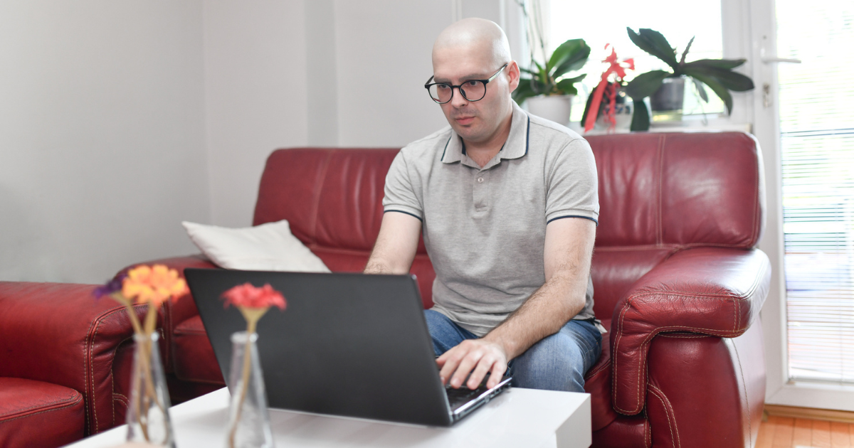 Male cancer patient sitting on the couch looking at laptop