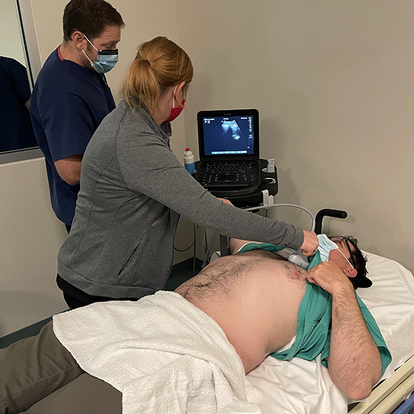 Two folks using an ultrasound on a man lying down on a bed