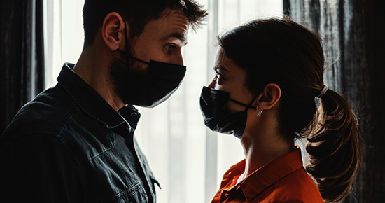 A man and a woman standing very near each other with masks on. 