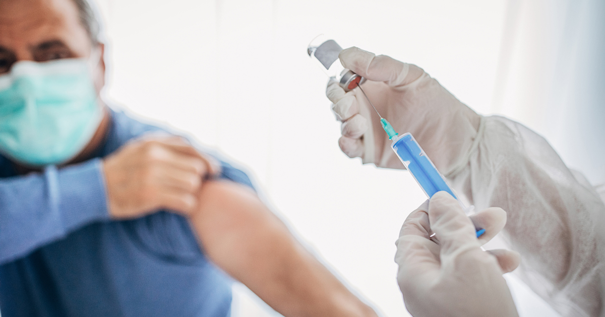 picture of a man in a mask rolling up his sleeve for his vaccination