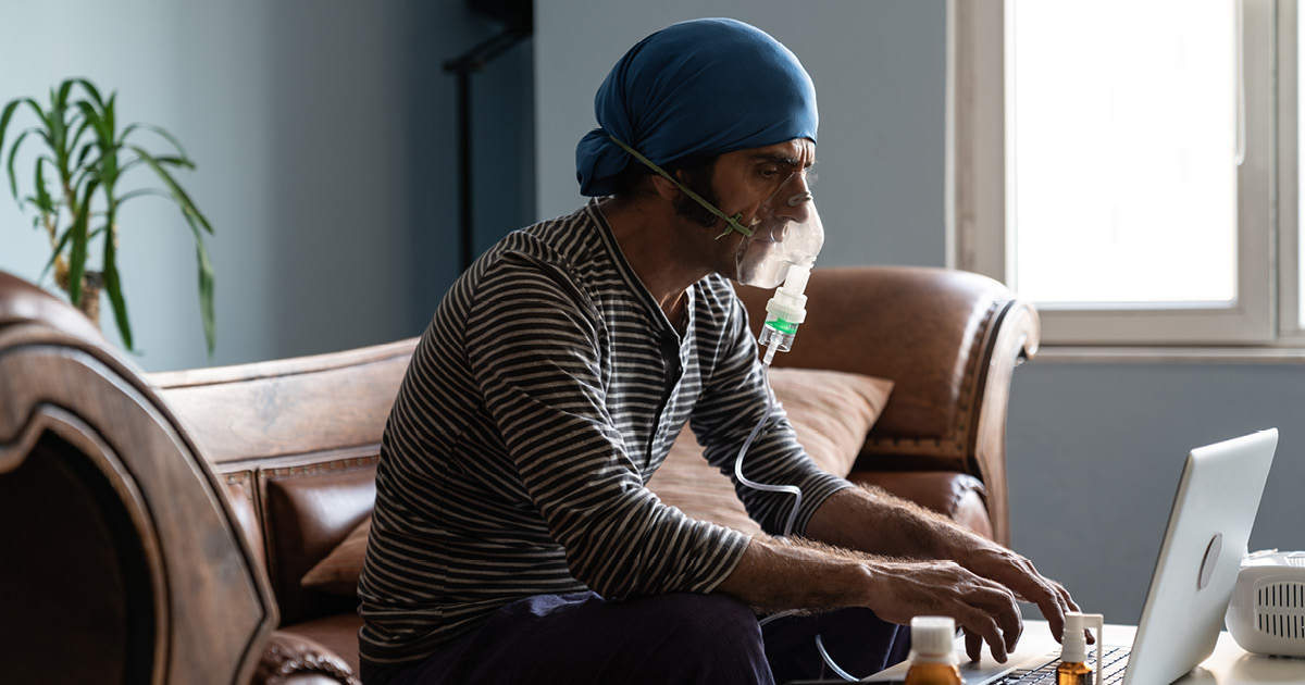 Man breathing with a nebulizer while on a laptop.