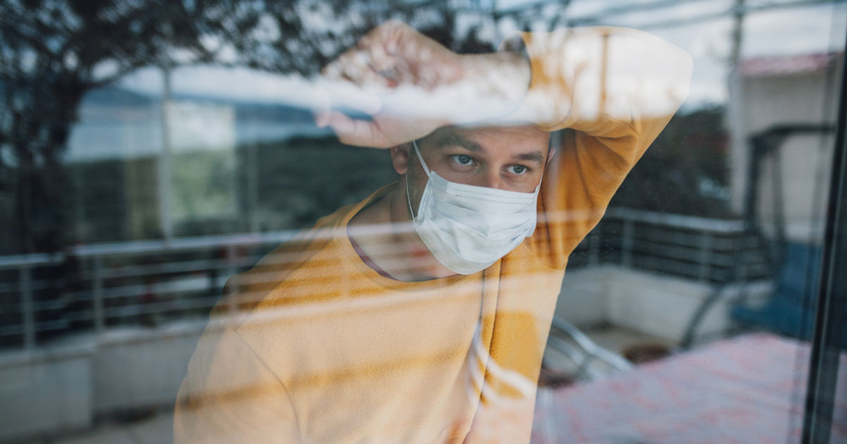 Person wearing a mask looking out a window