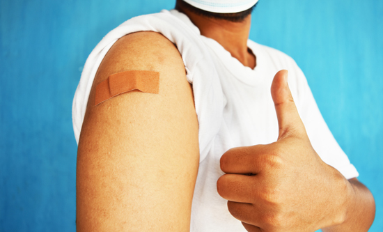 Asian man with a bandage on the arm, holding up a thumbs up
