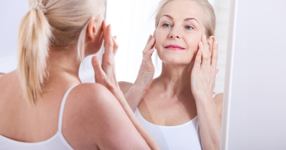 Woman looking at skin in mirror.