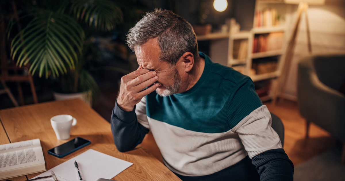 Man sitting at desk, rubbing his eye