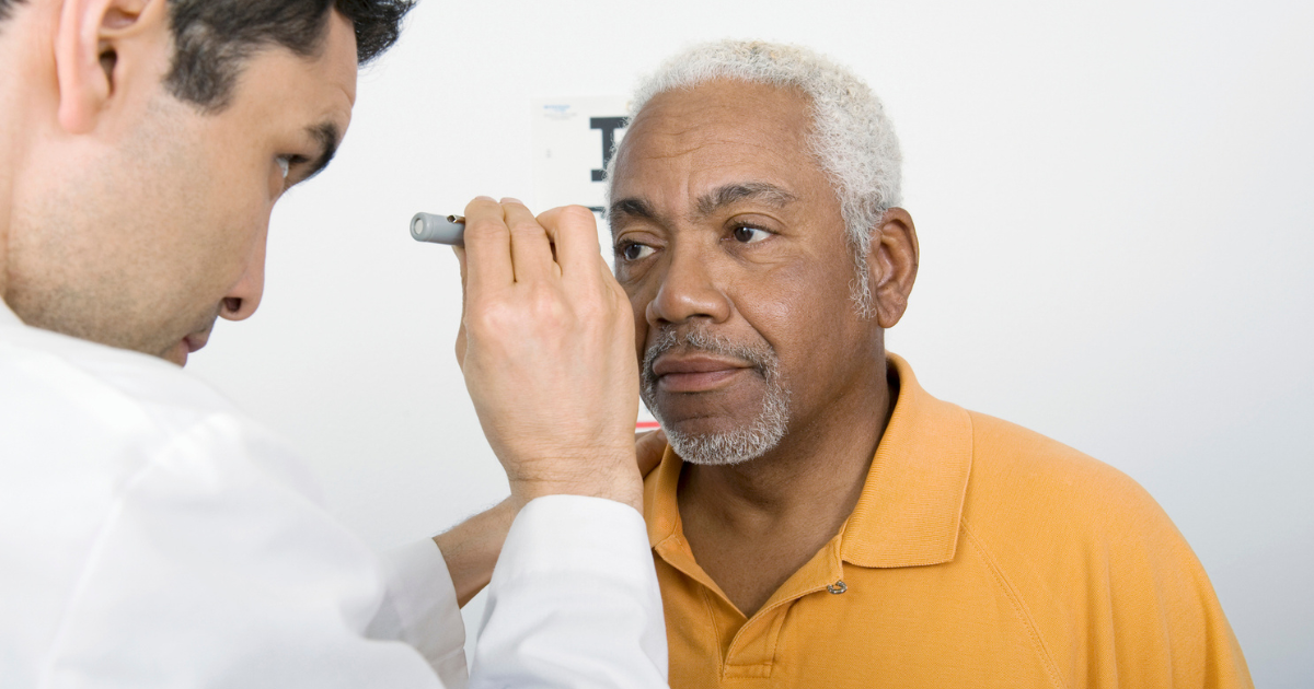 Eye doctor shining light in older man's eyes