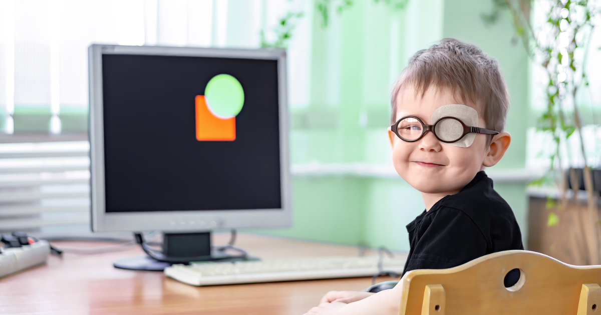 Young boy with patch over left eye and glasses sitting at computer