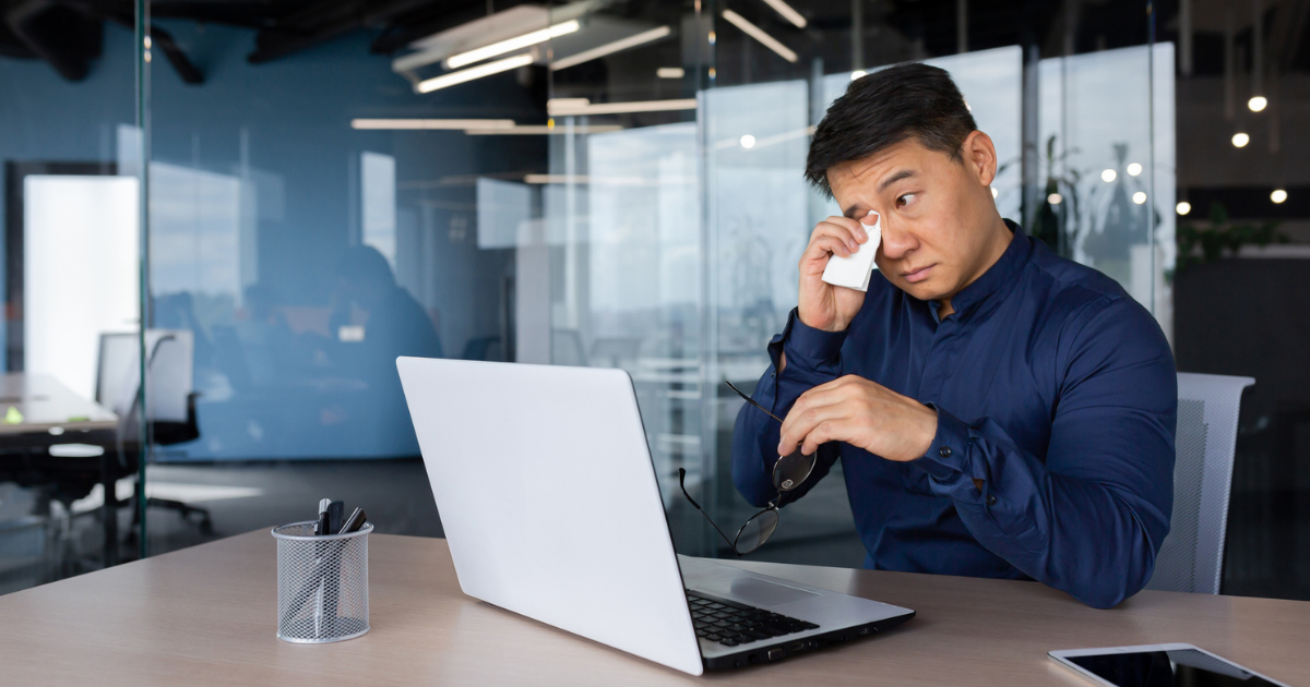 Man sitting at desk, wiping eyes with a tissue