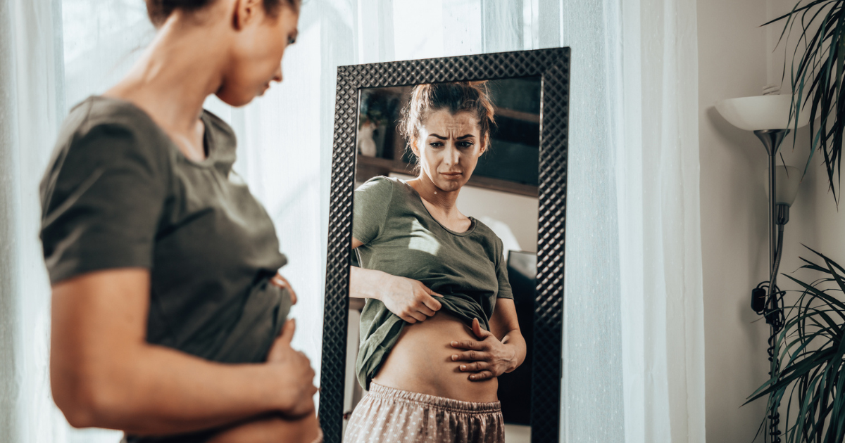 Woman looking at stomach in mirror