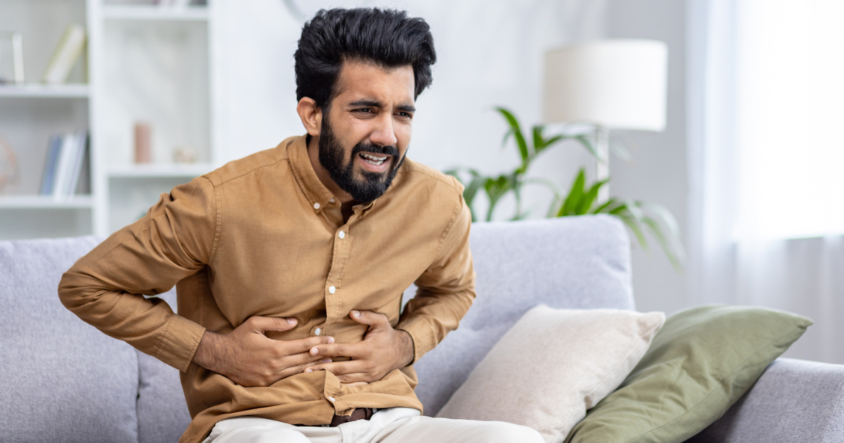Man sitting on couch, holding abdomen in pain