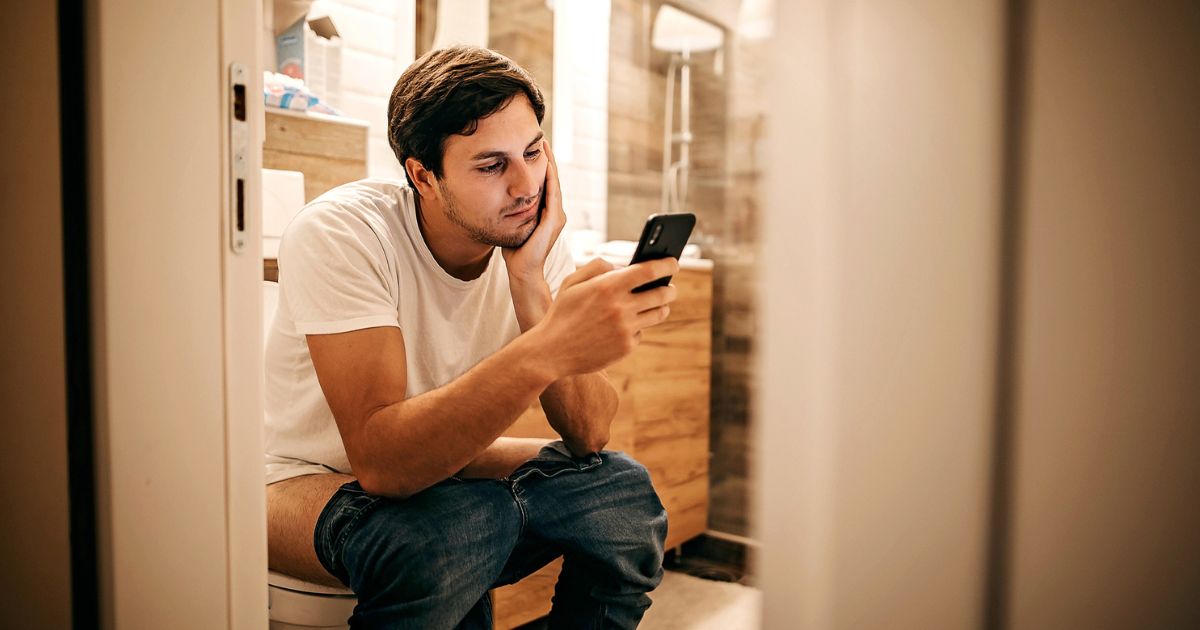 Man sitting on the toilet looking at his phone