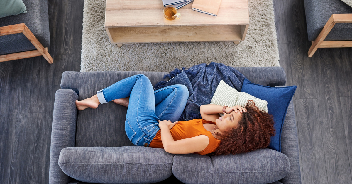 Woman holding her stomach laying on her couch