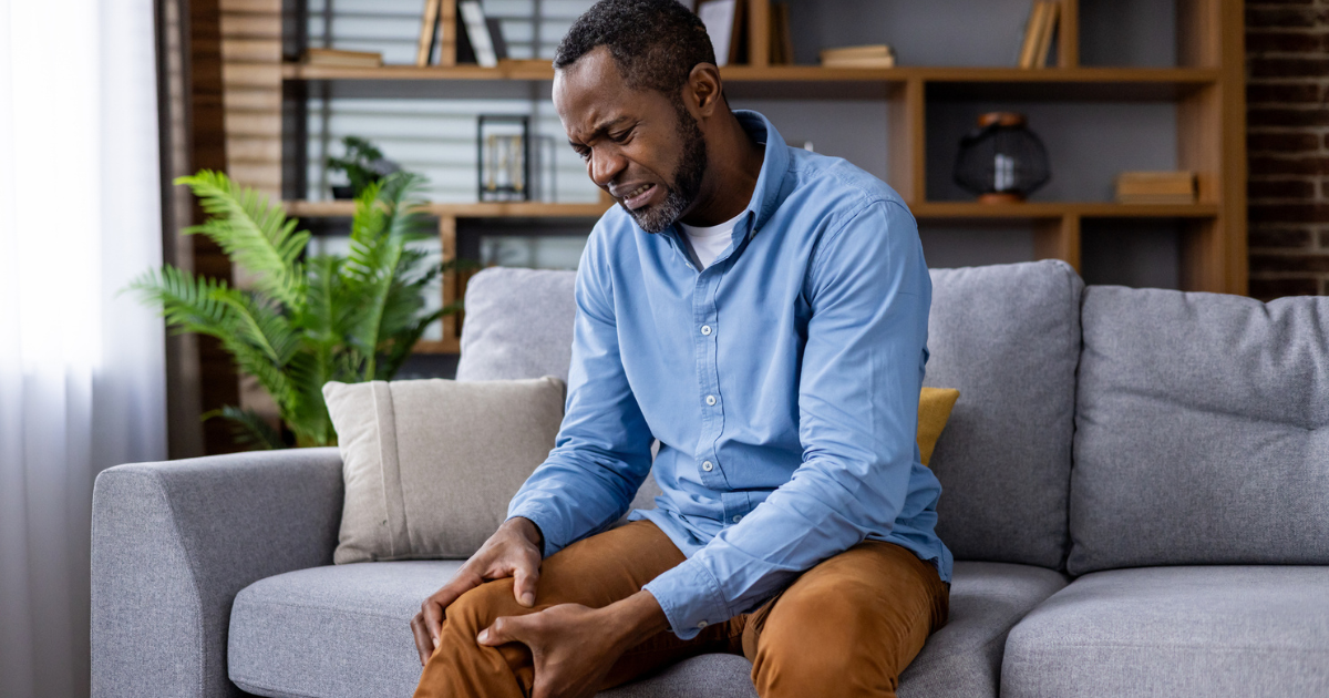 Man sitting on couch, holding leg in pain