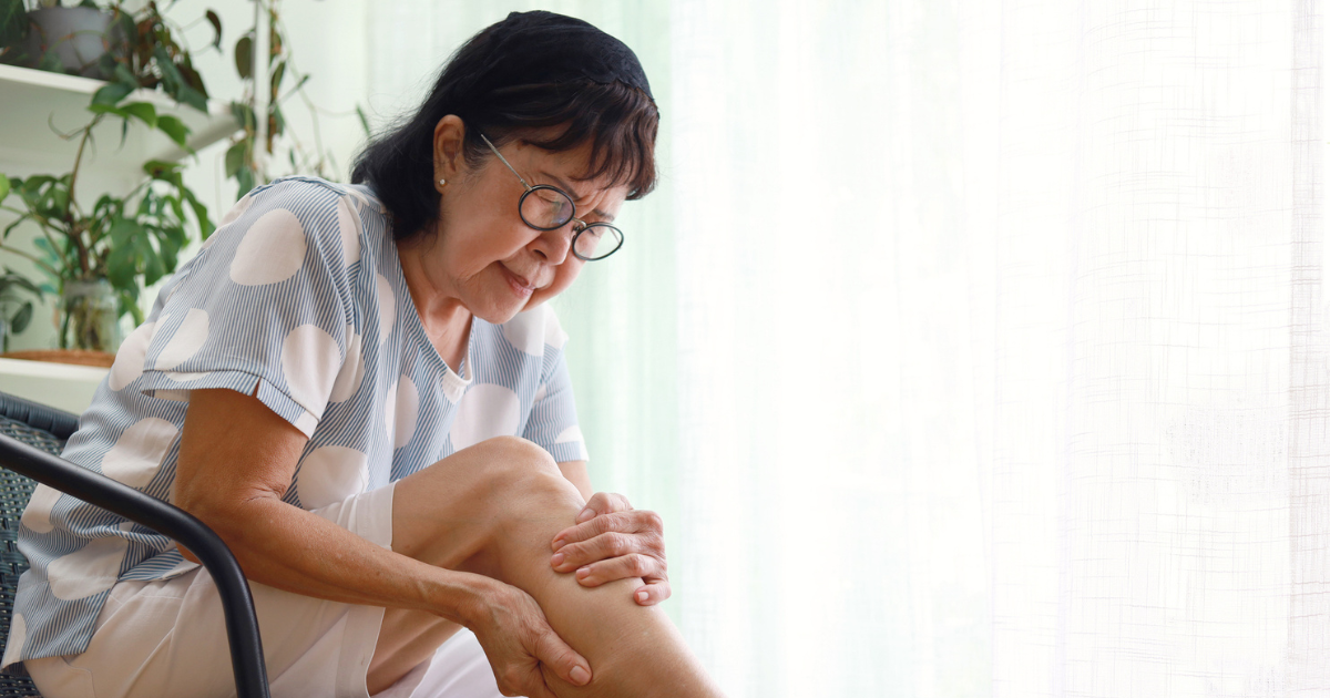 Older woman sitting, holding her leg in pain