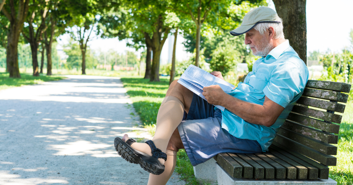 Man wearing compression socks, sitting on park bench reading