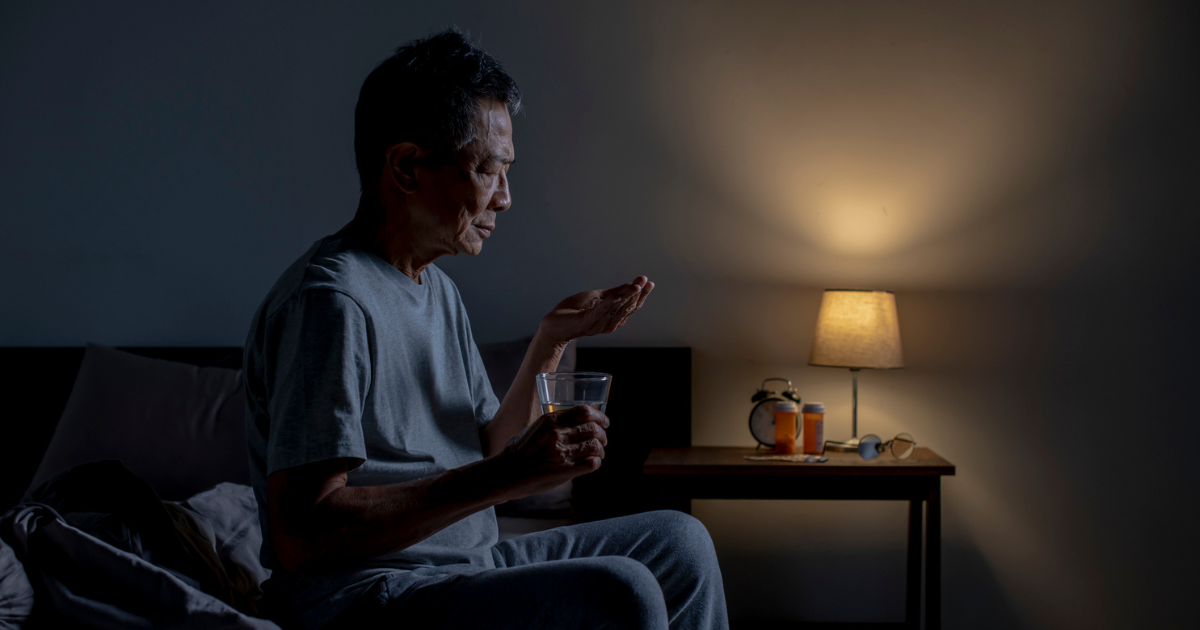 Older man sitting up in bed taking a pill