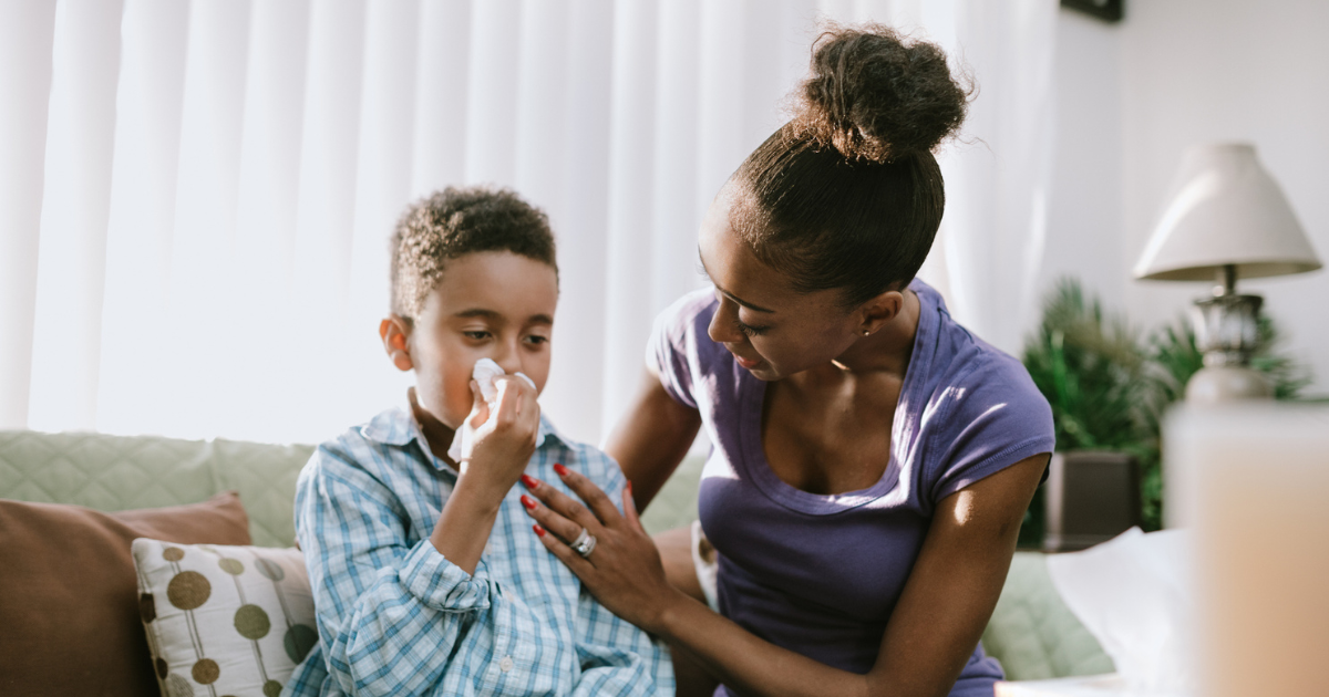 Child sitting on the couch with his mother, blowing his nose