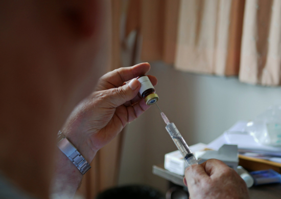An old man's hands carefully pulling the medicine into the syringe by himself at home