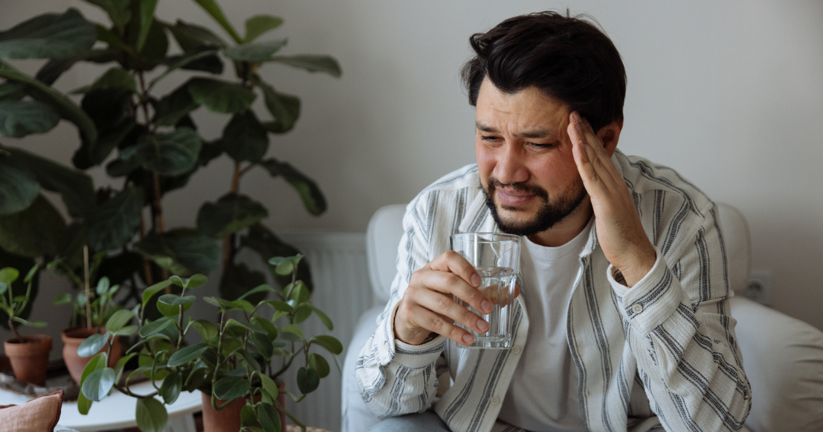 Man holding his head in pain holding a glass of water