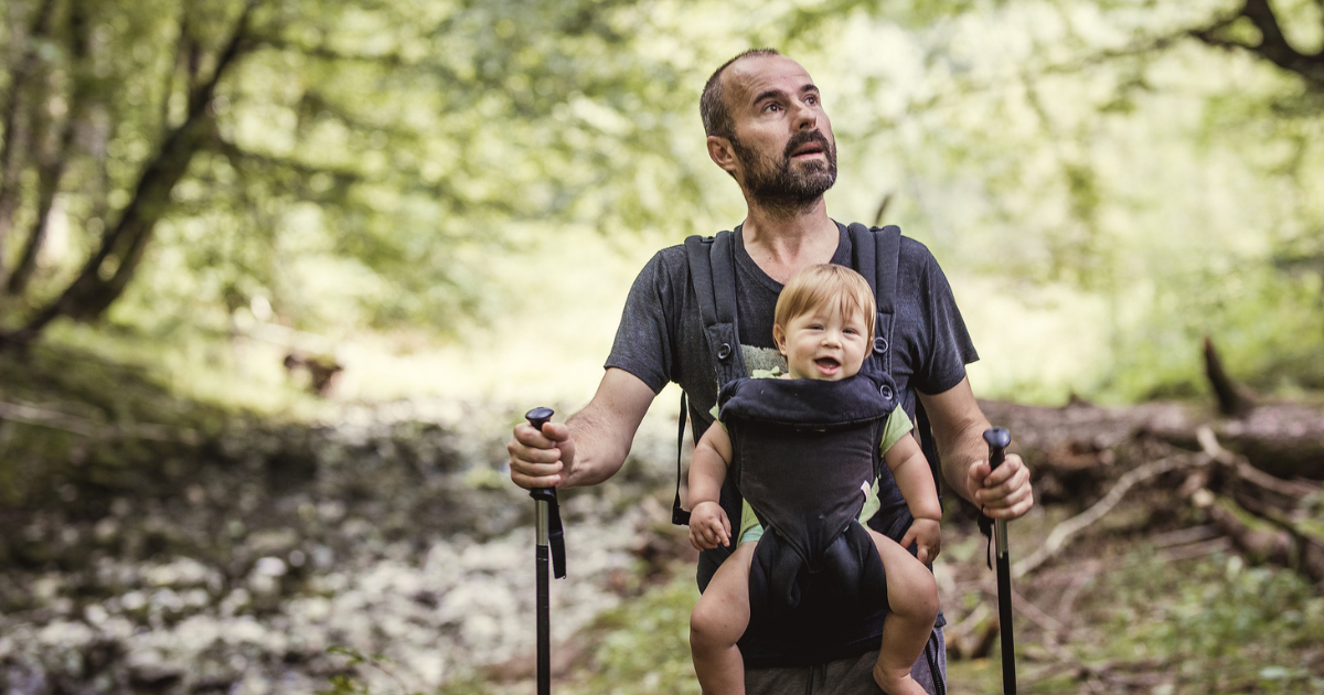 Man wearing a baby in a carrier, hiking in the woods