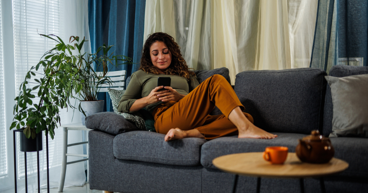 Barefoot woman lying on couch on her phone