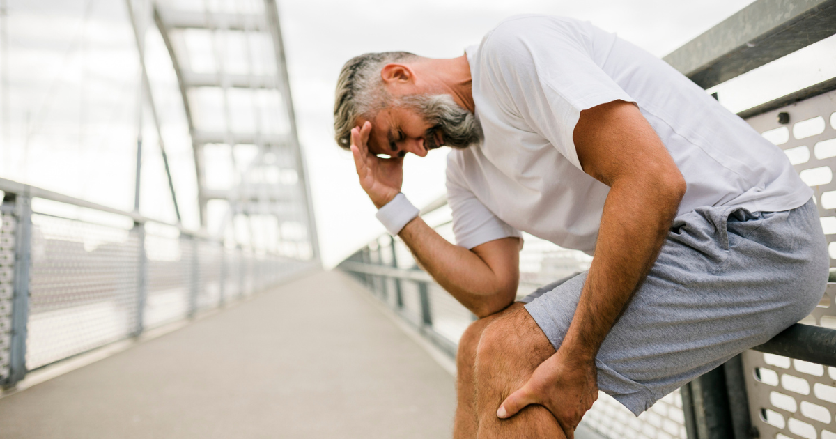 Man leaning against fence, holding his calf in pain