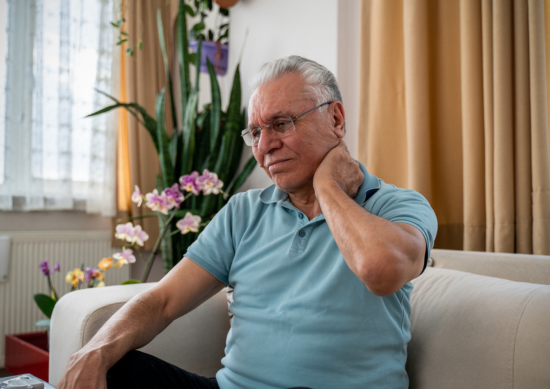 Man sitting on couch, holding neck in pain