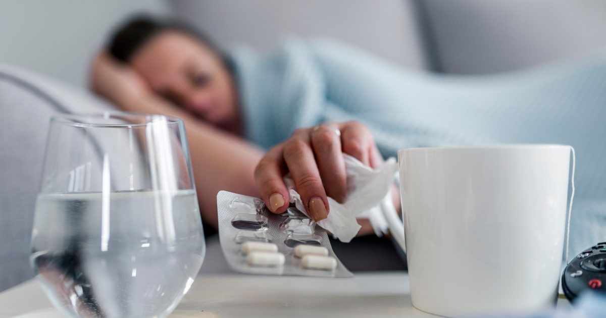 Sick woman laying on the couch, reaching for medicine