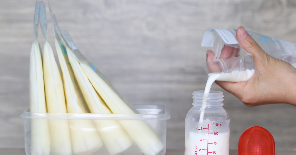 Close up of a hand pouring breast milk from a storage bag into a baby bottle