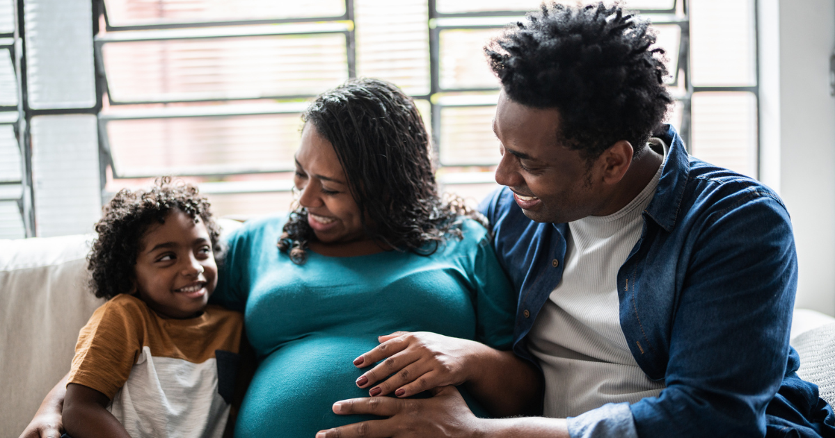 Father, pregnant mother, and young son sitting on couch