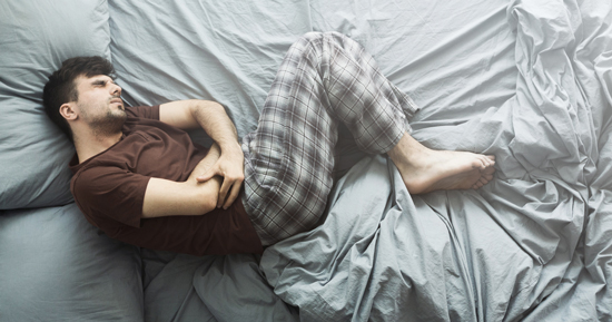 picture of a man clutching his stomach in bed