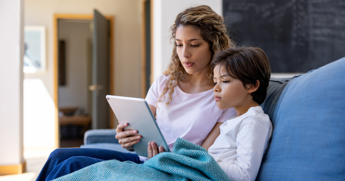 Mother and young son sitting on couch using a tablet for a telehealth appointment
