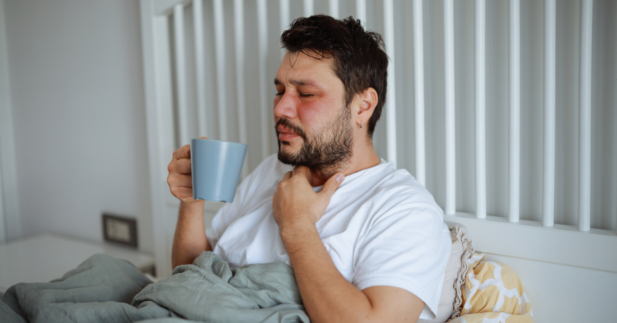 Sick man sitting in bed holding a mug