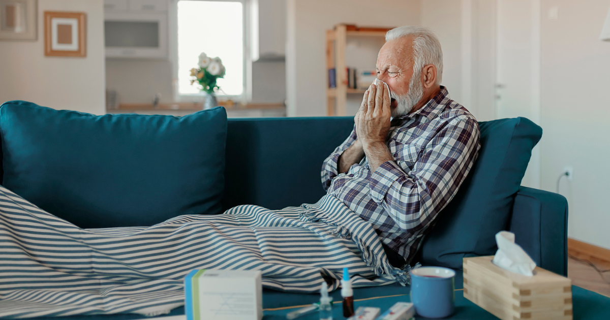 Older man laying on the couch blowing his nose