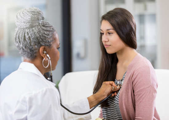 Doctor listening to the heartbeat of a young woman with a stethoscope